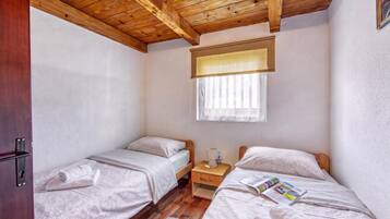 Een knus slaapkamer met twee eenpersoonsbedden, een houten plafond, een raam met zonwering en een nachtkastje met een lamp.