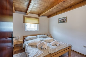A bedroom with a wooden ceiling, a bed with a patterned bedspread, two bedside tables with lamps, and a window with a blind.