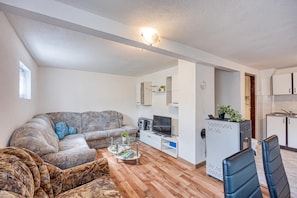 A living room with a sofa, a coffee table, a TV, and a small kitchen area with cabinets and a refrigerator.