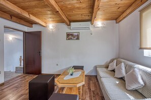 A room with a wooden ceiling, a sofa, a table with a plant, and a picture on the wall.