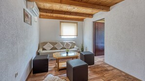 A room with a wooden ceiling, a sofa with cushions, a glass coffee table, two black ottomans, and a wooden floor.