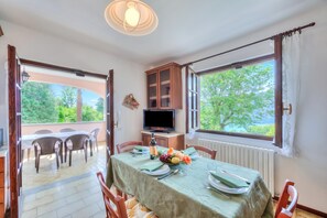 A dining area with a table set for four, a television on a stand, and a view of greenery outside.