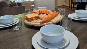 Una mesa de comedor dispuesta con pan, un bol y vasos, con un ventilador de techo y un televisor al fondo.