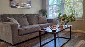 Una sala de estar con un sofá, una mesa de centro, un cuadro en la pared y una ventana con persianas.