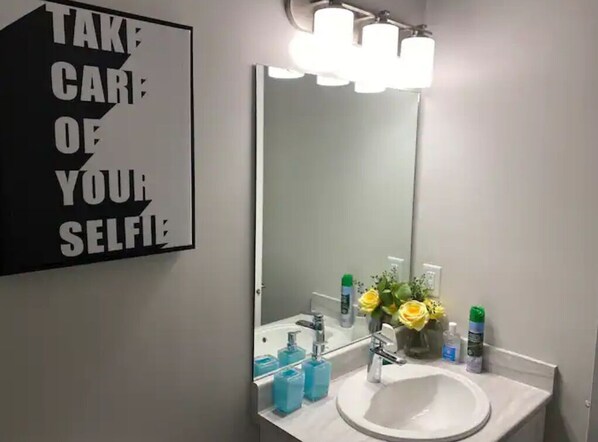 A bathroom with a sink, mirror, and toiletries. A sign on the wall reads "TAKE CARE OF YOUR SELFIE".