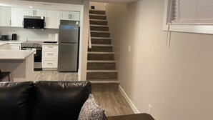 A modern kitchen with white cabinets, a stainless steel refrigerator, and a microwave. There is a staircase leading to another level.