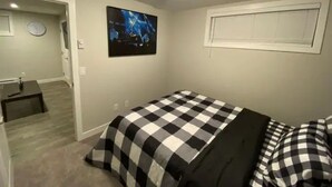 A bedroom with a checkered bedspread, a clock on the wall, and a framed picture.