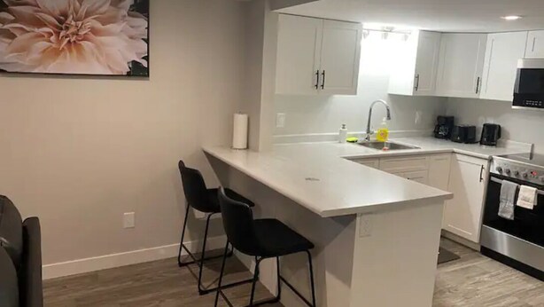 A modern kitchen with white cabinets, a stainless steel stove, and a bar area with two black barstools.