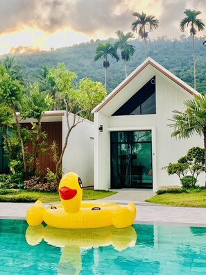 Una casa moderna con piscina, rodeada de vegetación exuberante y palmeras.