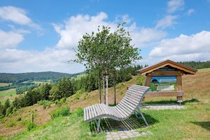 A wooden bench, a wooden structure with a sign, and a tree in a hilly landscape. - Apartment 'Ferienwohnung' with Mountain View, Shared Garden and Wi-Fi (Ibach)