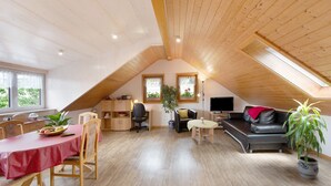 Et rummeligt loftrum med spiseplads, sofa, fjernsyn og en potteplante.