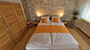 A bedroom with a large bed, wooden wardrobe, stone wall, bedside lamps, and a potted plant. - Holiday Apartment 'Albfewo' with Terrace, Garden and EV Charging Station (St. Johann)