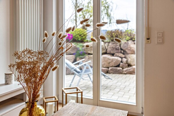 A room with a large window, a vase with dried plants, a wooden table, and a chair.