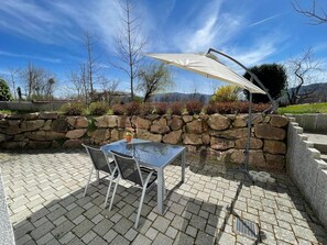 Une terrasse avec une table et des chaises, un mur en pierre et une vue sur les arbres et les montagnes.