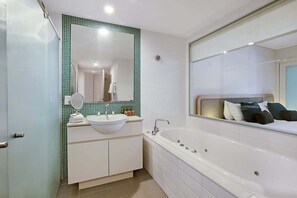 Ein modernes Badezimmer mit Waschbecken in Weiß, einem großen Spiegel, einer Badewanne und einer Wand mit grünen Fliesen.