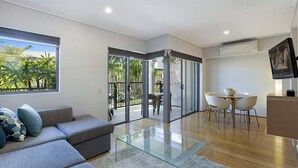 Ein modernes Wohnzimmer mit einem Glastisch, einem grauen Sofa und einem Essbereich mit weißen Stühlen.