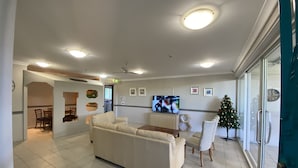 A spacious living area with a large sofa, a dining table, and chairs. There is a television mounted on the wall, and a Christmas tree is visible near the window. - Homely Inn Queen Street (Southport)
