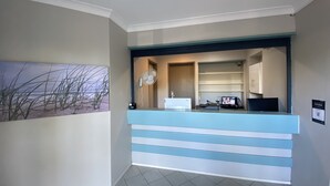 A reception area with a counter, a desk, a computer, and a painting of grass on the wall. - Homely Inn Queen Street (Southport)