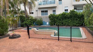 A swimming pool with a black fence, surrounded by greenery and a brick pathway. - Homely Inn Queen Street (Southport)