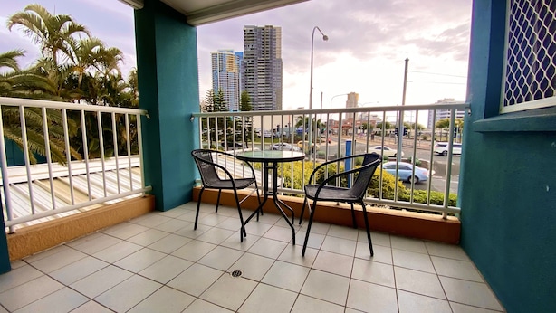 A balcony with two chairs and a table, overlooking a street with cars and buildings. - Homely Inn Queen Street (Southport)