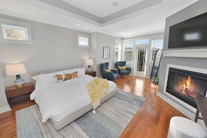 A bedroom with a bed, bedside tables, a fireplace, and a view of the outdoors. - Mount Finlayson View Villa (Victoria)