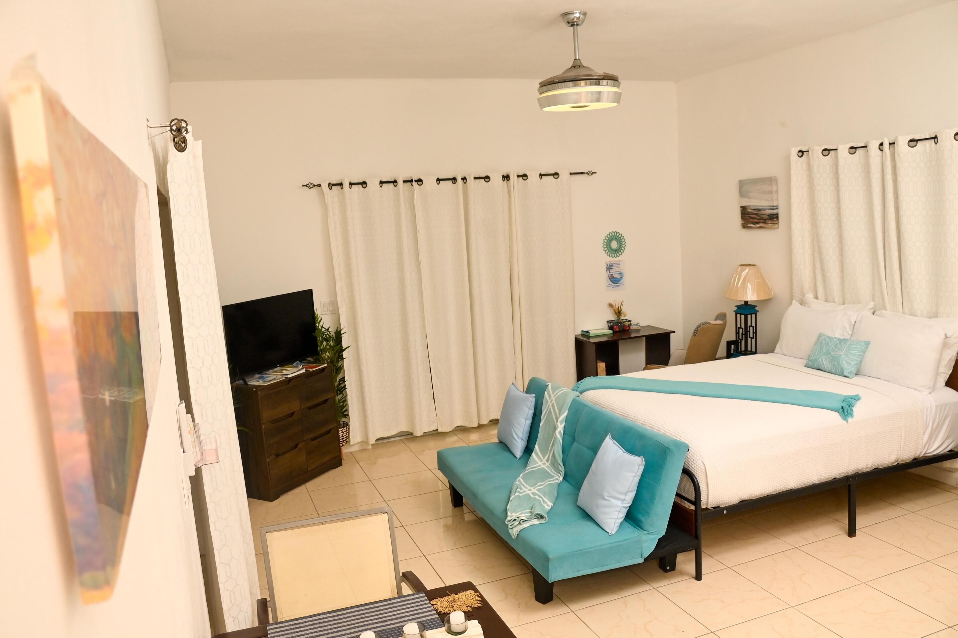 A hotel room with a bed, a sofa, a TV, a lamp, and a small table.