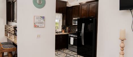 Una cocina con armarios de madera oscura, un refrigerador negro, un microondas y un suelo estampado.