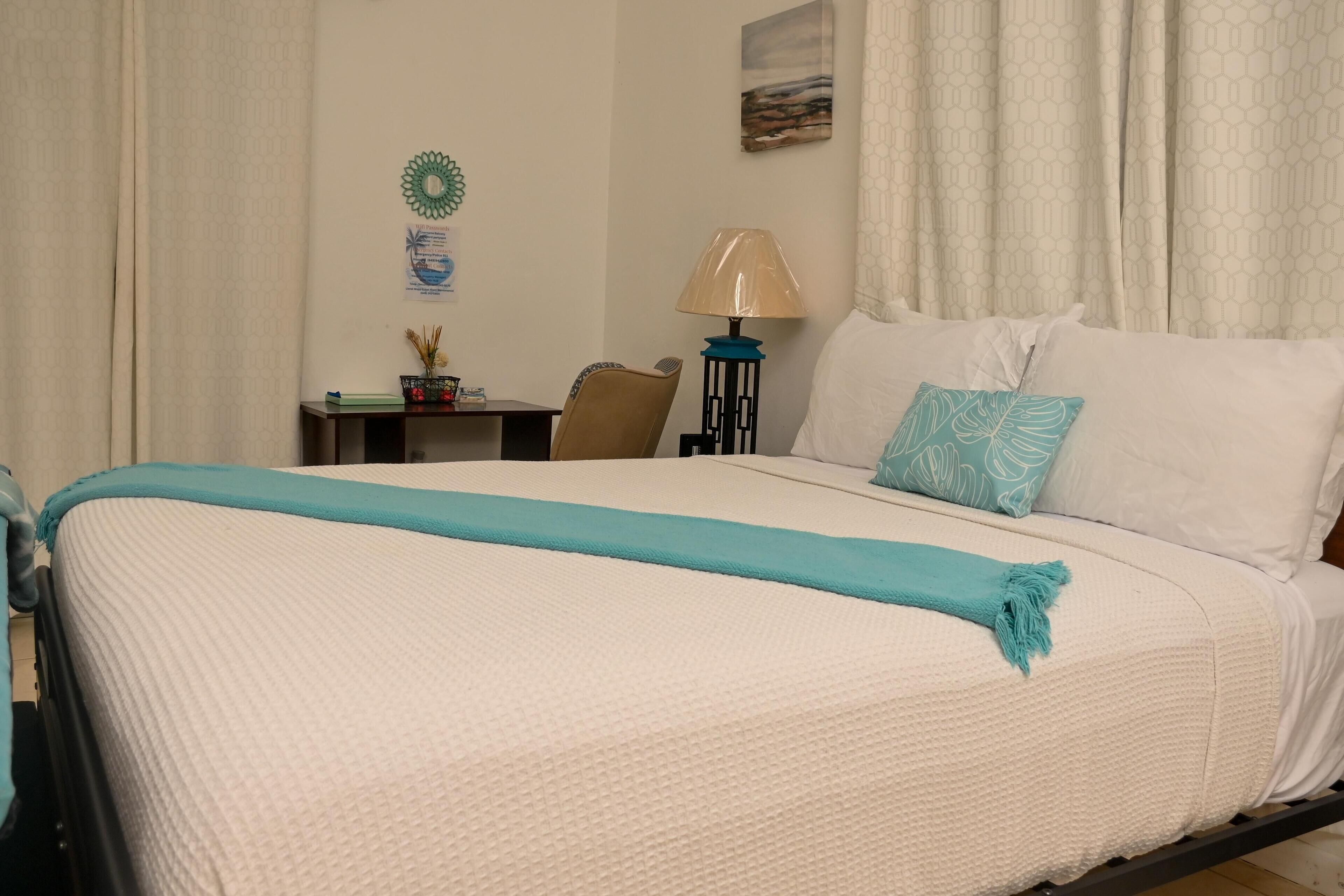 A hotel room with a large bed, a desk, a chair, a lamp, and a wall decoration.