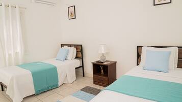 A bedroom with two beds, a nightstand, a lamp, and a window with curtains.
