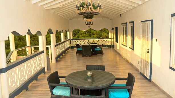 A covered outdoor patio with a round table and chairs, a chandelier, and a view of greenery.