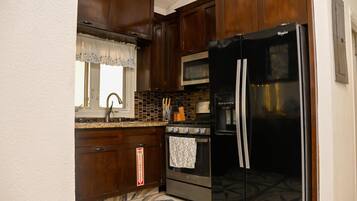 A kitchen with dark wooden cabinets, a stainless steel refrigerator, a microwave, and a stove.