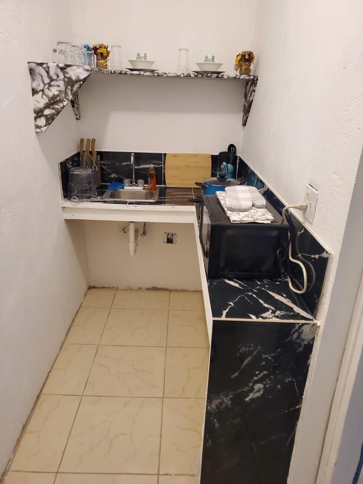 A small kitchen with a sink, countertop, and a shelf above.