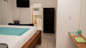 A bedroom with a bed, a TV mounted on the wall, a wooden cabinet, and a small table with books and a candle.