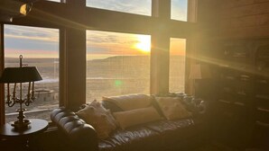 Una habitación con sofá de cuero frente a un ventanal con vista al mar al atardecer.
