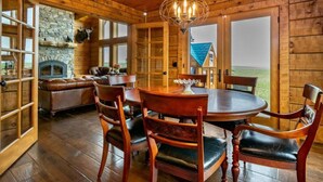 Interior de madera con chimenea de piedra, una mesa de comedor con sillas y vistas al exterior.