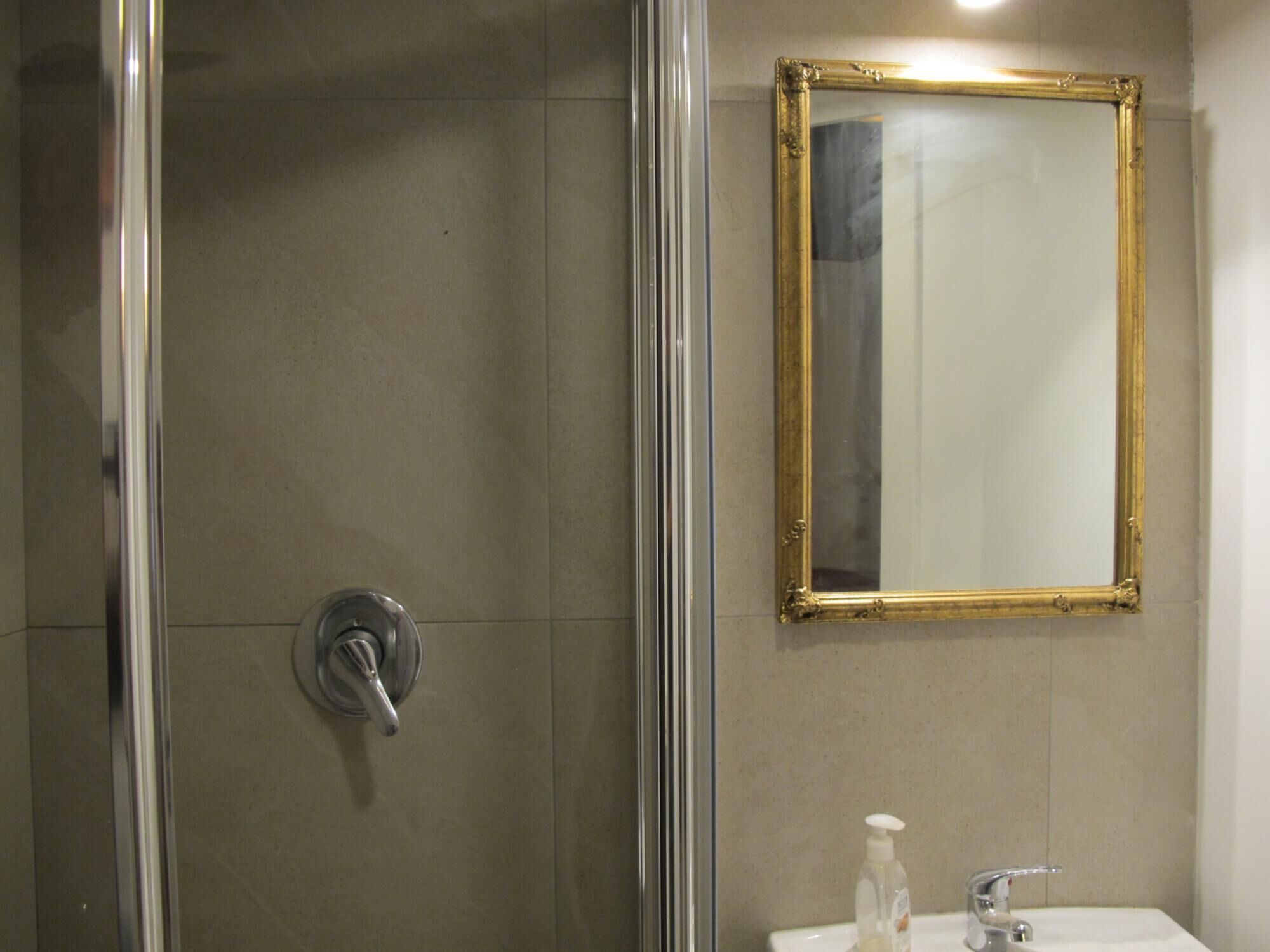 A bathroom with a glass shower enclosure, a sink with a mirror, and a soap dispenser.