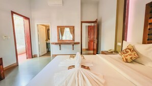 Quarto de hotel com cama, mesa de cabeceira com telefone, espelho e banheiro visível por uma porta aberta.