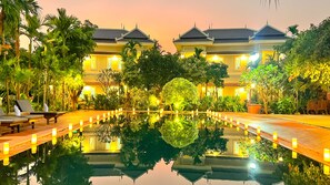 A pool with a reflection of a building and trees, surrounded by a well-lit garden area. - SANNA VILLA Residence (Siem Reap)