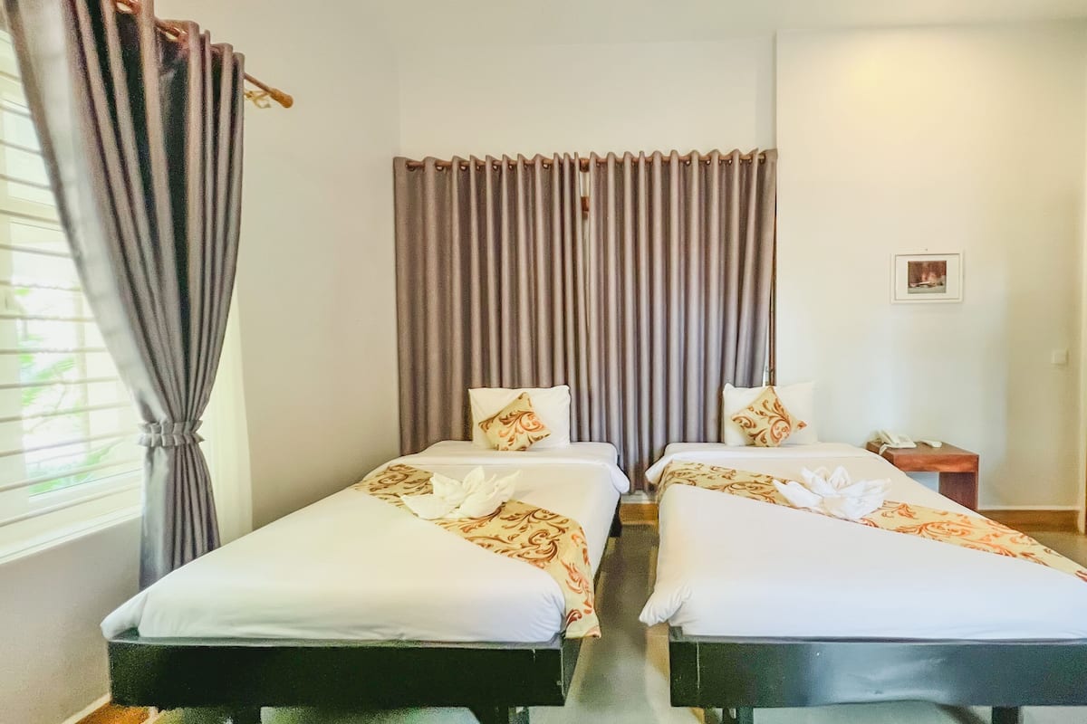 Una habitació d'hotel amb dos llits, una taula de nit, un mirall i una finestra amb cortines.