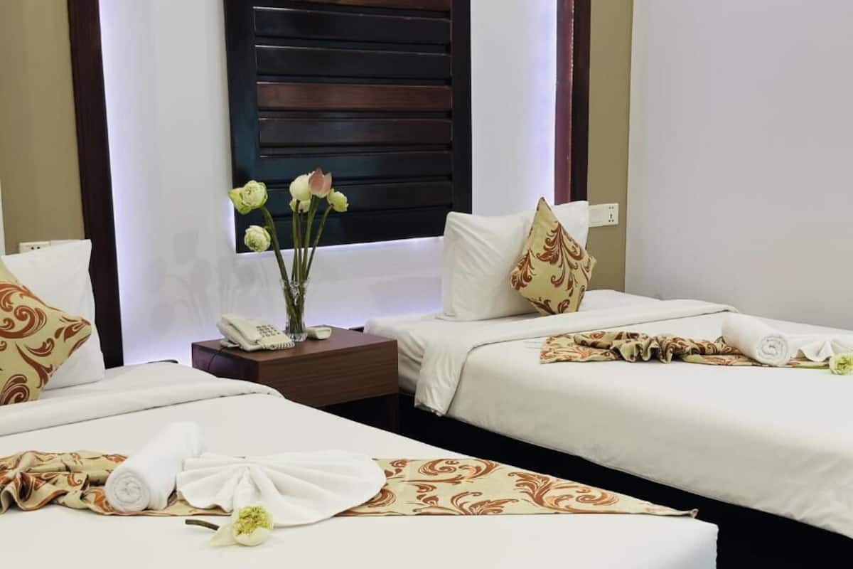 Habitació d'hotel amb dos llits, una petita taula de nit amb un telèfon, un vas amb flors i una finestra amb persianes.