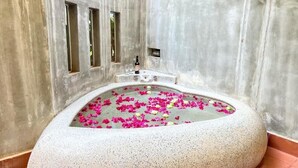 Uma banheira cheia de água e pétalas de rosa, com uma garrafa e um copo na borda.