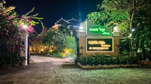 A well-lit entrance with a sign for Sanna Villa Resort & Spa, surrounded by lush greenery and flowering plants. - SANNA VILLA Residence (Siem Reap)