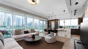 A modern living room with a sofa, coffee table, and a city view through large windows. - Maison Privee - Deluxe 3BR Apt w/ Dubai Marina View and Beach Access (Dubai)