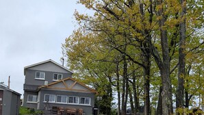 Ein zweistöckiges Haus mit Garage, einer Veranda mit Stühlen und einem großen Baum mit gelben Blättern.