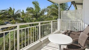 Een balkon met een witte reling, een ronde tafel en rieten stoelen.