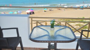 Un balcó amb taula i cadires de vidre, amb vista a una platja plena de paperiges i gent.