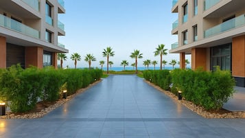 Un hotel moderno con un camino central bordeado por exuberante vegetación y palmeras, que conduce a una playa.