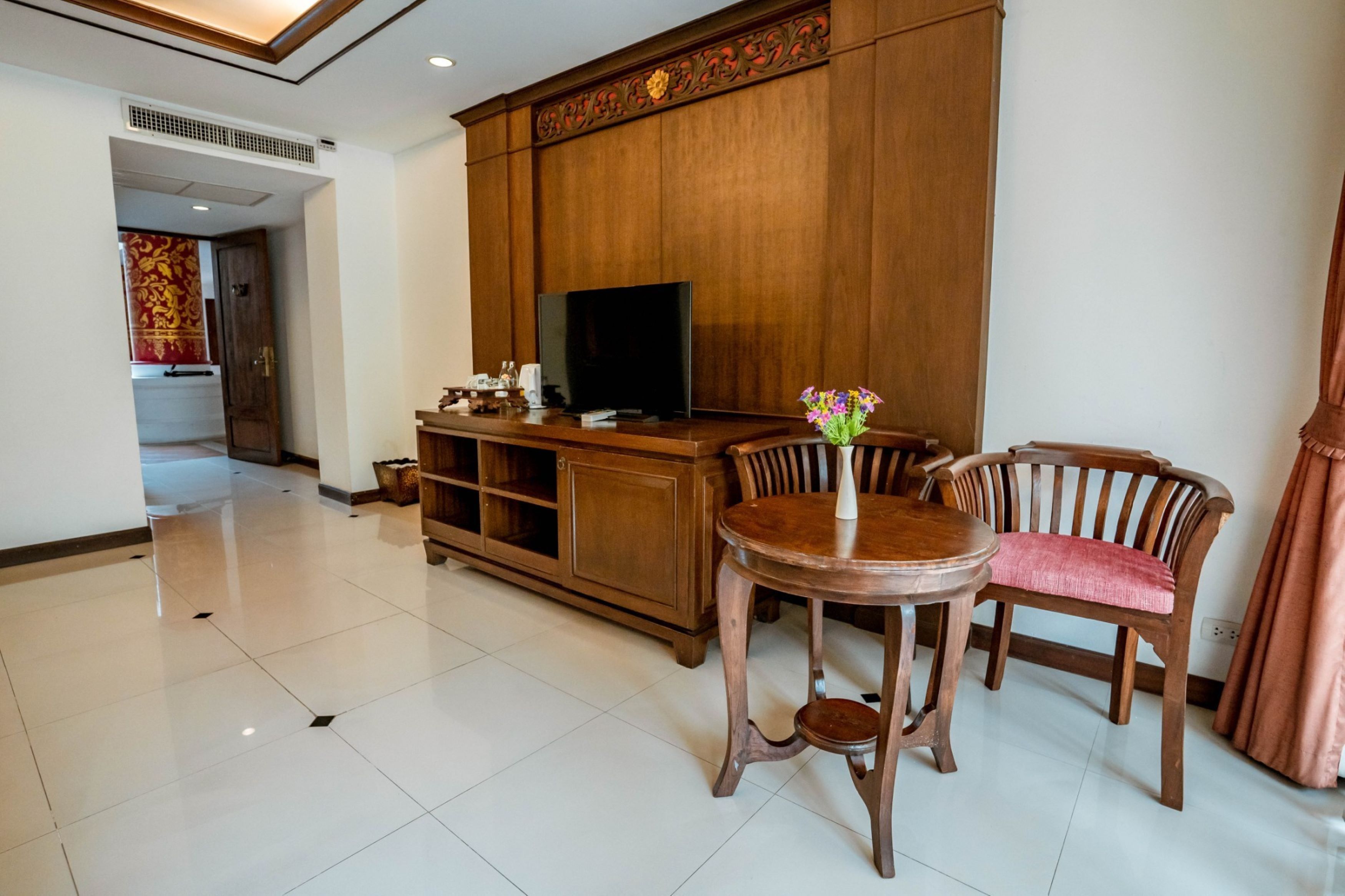A hotel room with a wooden cabinet, a television, a round table, and two upholstered chairs.