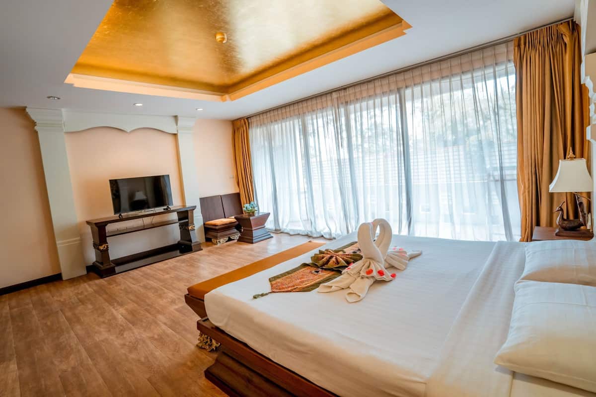 Una habitación de hotel con una cama grande, televisión, escritorio y ventana con cortinas.