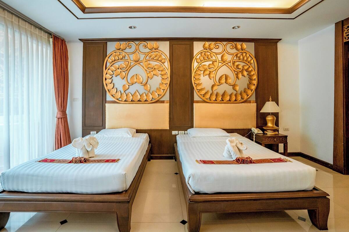 Habitación de hotel con dos camas, un panel decorativo grande en la pared, una lámpara de noche y un ventanal con cortinas.